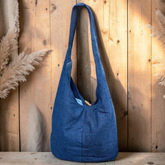 Bidora blue denim hobo shoulder bag with a slouchy silhouette and rustic wooden toggle closure against wood backdrop.