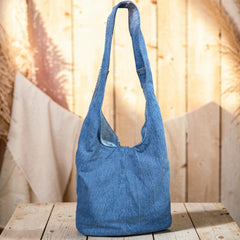 Bidora denim hobo shoulder bag with a slouchy silhouette and wide strap, displayed on a rustic wooden surface.