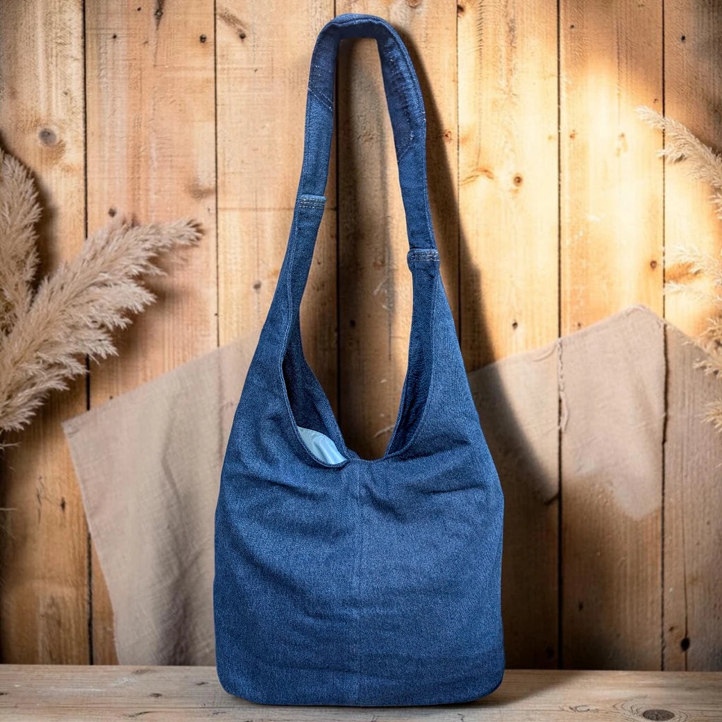 Bidora indigo denim hobo shoulder bag with a slouchy silhouette and sturdy strap against a rustic wooden background
