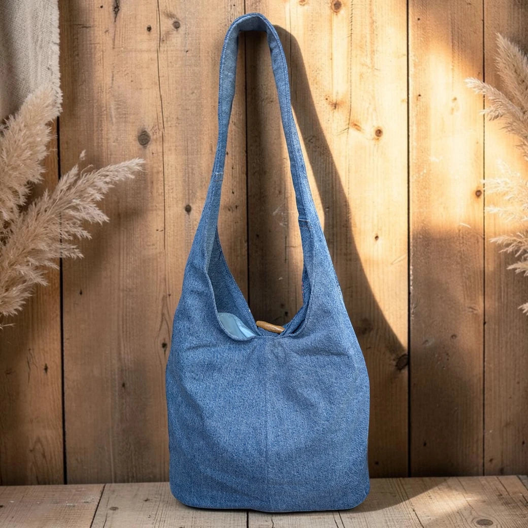 Bidora denim hobo shoulder bag with a slouchy silhouette and rustic wooden toggle closure against a wooden background.