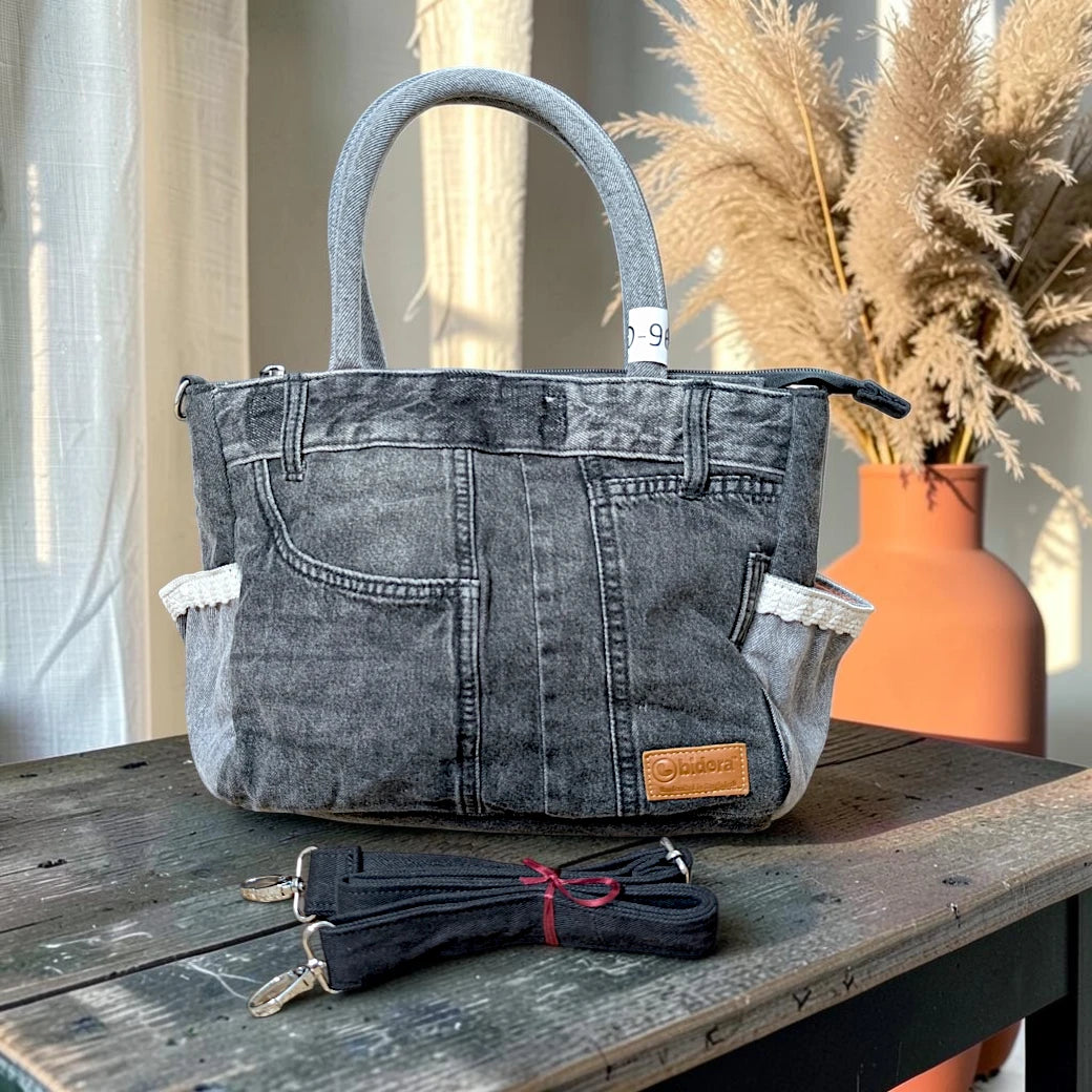 Bidora washed-grey denim handbag with patchwork design, lace trim, and a detachable black shoulder strap on a table.