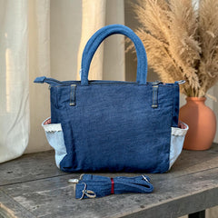 Bidora upcycled denim handbag with patchwork details, sturdy handles, and a detachable shoulder strap on a wooden table