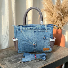 Bidora handcrafted blue denim tote bag with brown side panels, white lace trim, and a detachable shoulder strap.