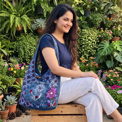 Bidora denim hobo bag with floral embroidery and butterfly motif, worn by a woman in a lush garden setting.