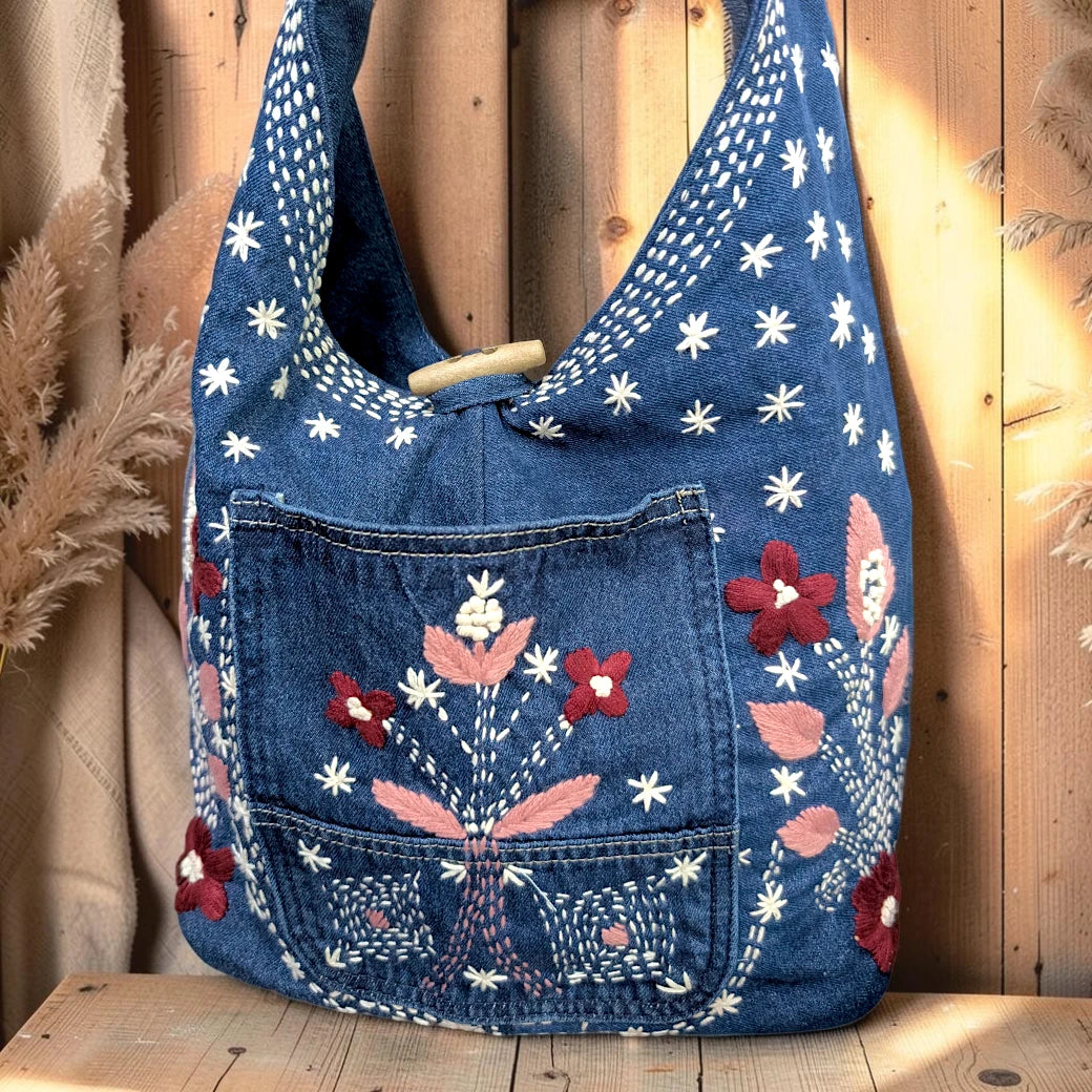 Bidora blue denim hobo shoulder bag with floral embroidery, front pocket, and rustic wooden toggle closure.