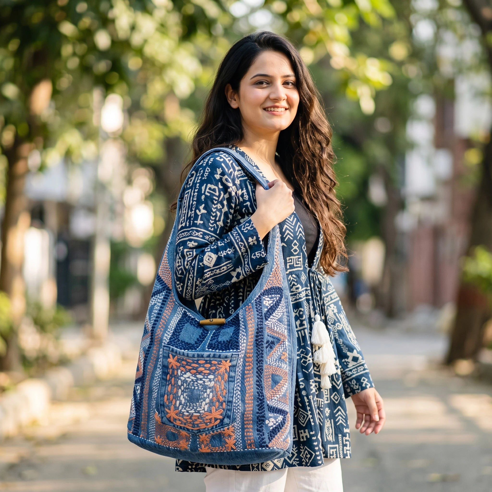 Bidora denim hobo shoulder bag with intricate embroidery and wooden toggle closure worn by a woman outdoors.