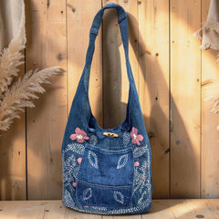 Bidora blue denim hobo bag with pink and white floral embroidery, front pocket, and rustic wooden toggle closure.