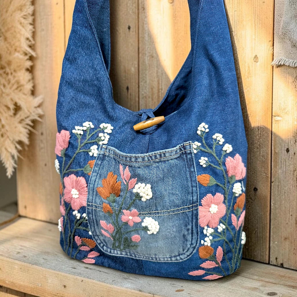 Bidora blue denim hobo shoulder bag with intricate floral embroidery, front pocket, and rustic wooden toggle closure.