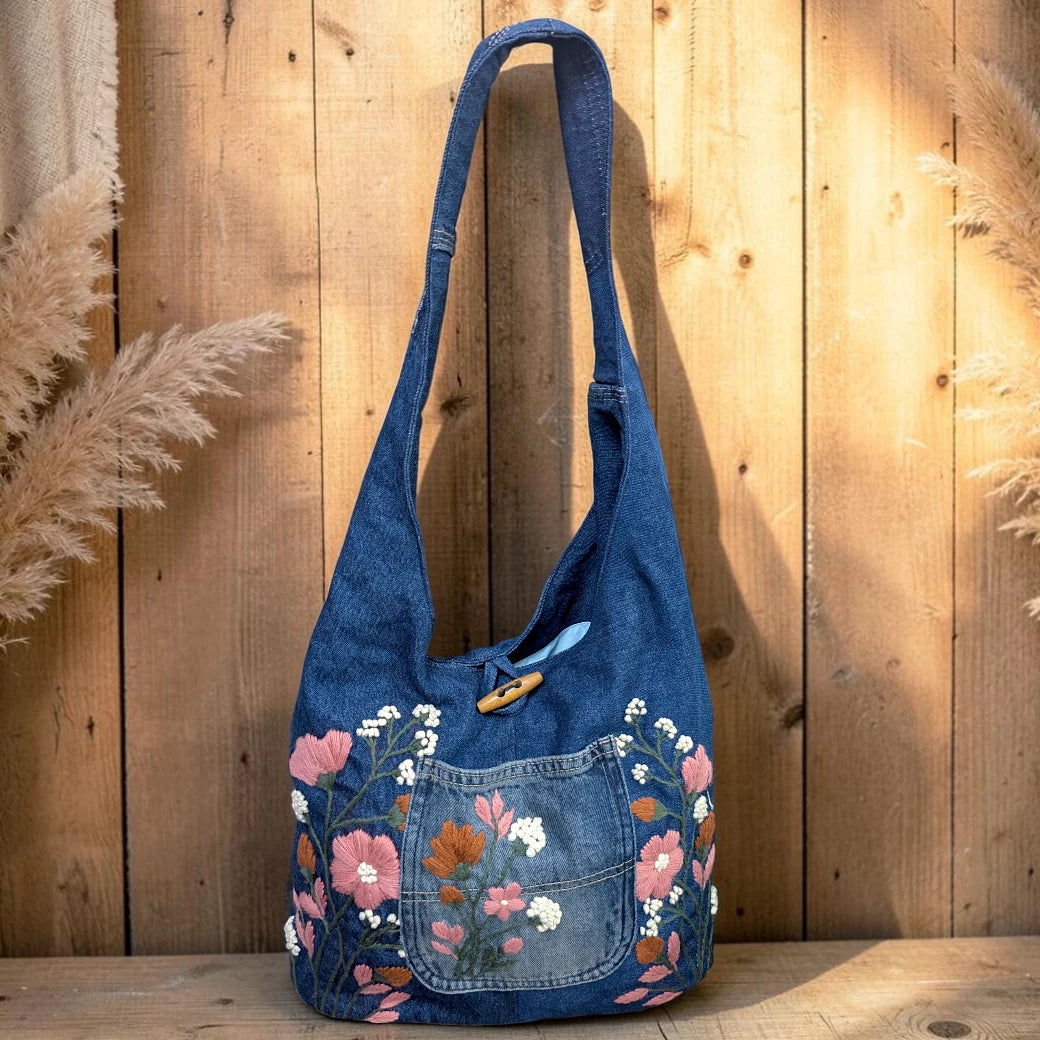 Bidora blue denim hobo shoulder bag with intricate floral embroidery, front pocket, and rustic wooden toggle closure.