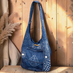 Bidora indigo denim hobo shoulder bag with white hand-stitched embroidery, wooden toggle closure, and front pocket.
