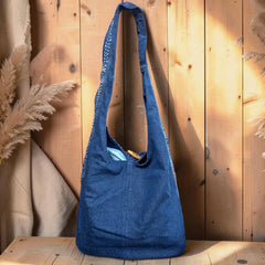 Bidora indigo denim hobo shoulder bag with intricate embroidery and a rustic wooden toggle closure on a wooden surface.