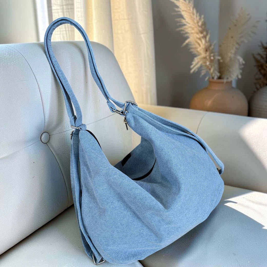 Bidora light blue denim hobo bag with an adjustable strap and slouchy silhouette resting on a white chair.