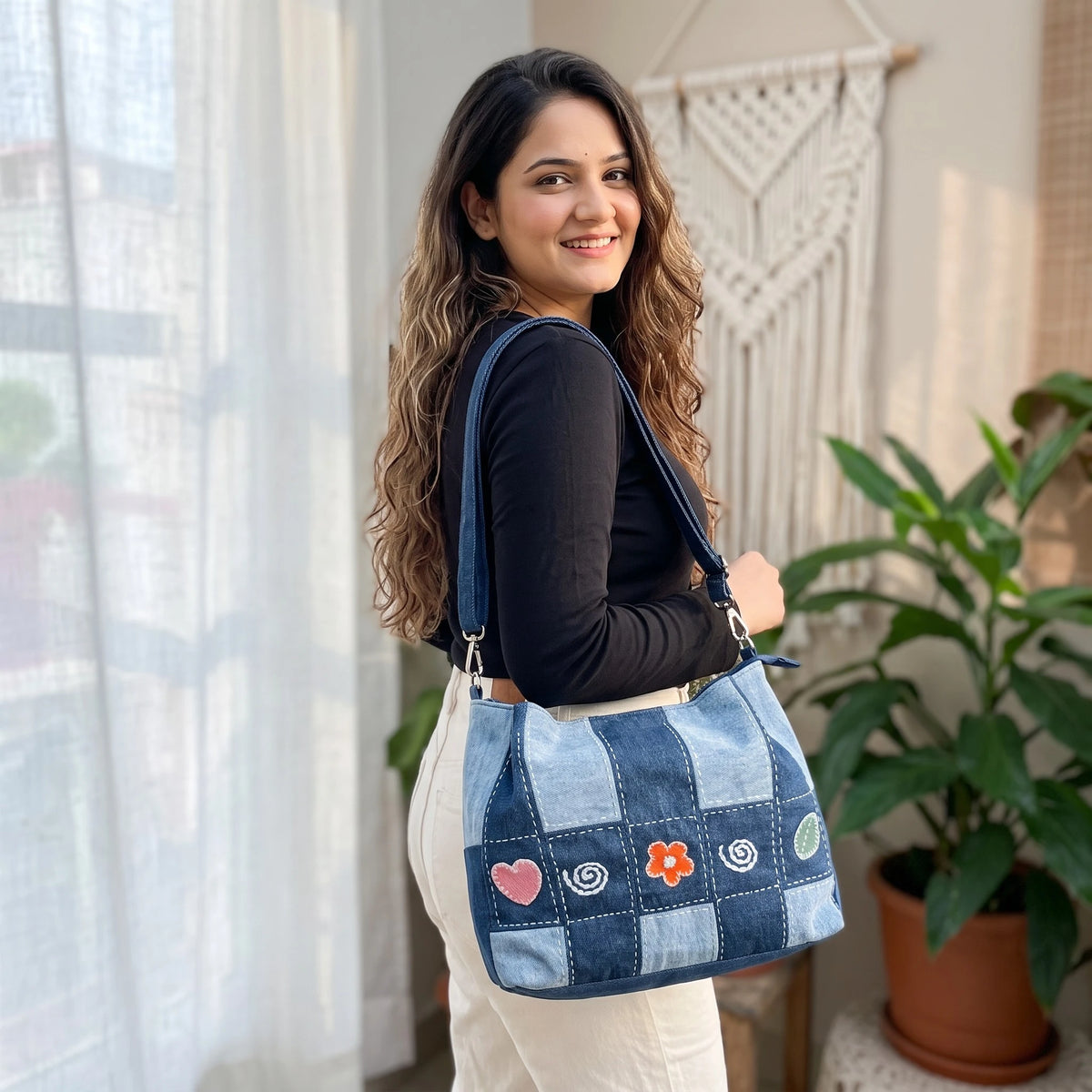 Bidora patchwork denim shoulder bag with embroidered heart and flower details worn by a woman in a bright room