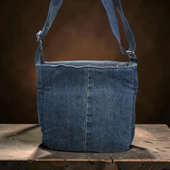 Bidora upcycled blue denim crossbody bag with an adjustable shoulder strap resting on a rustic wooden surface.