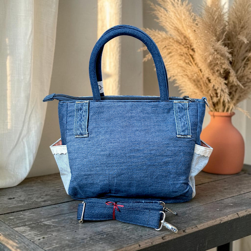 Bidora upcycled blue denim handbag with top handles, side pockets, and a detachable shoulder strap on a wooden table.