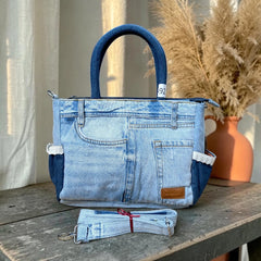 Bidora upcycled light-wash denim tote handbag with dark blue handles, exterior pockets, and detachable shoulder strap.